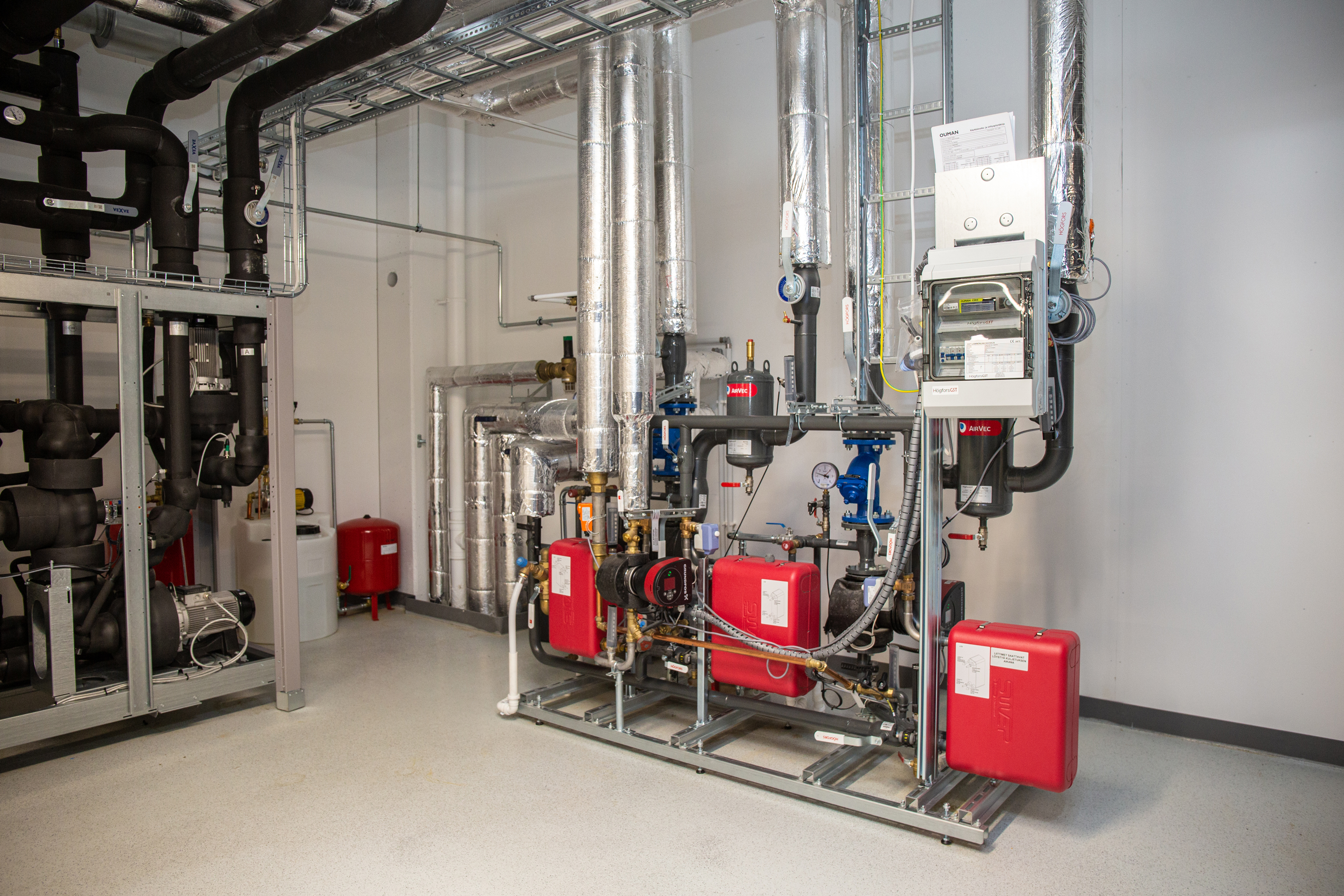 Heating system installation with pumps, insulated pipes and control cabinet in a building mechanical room.