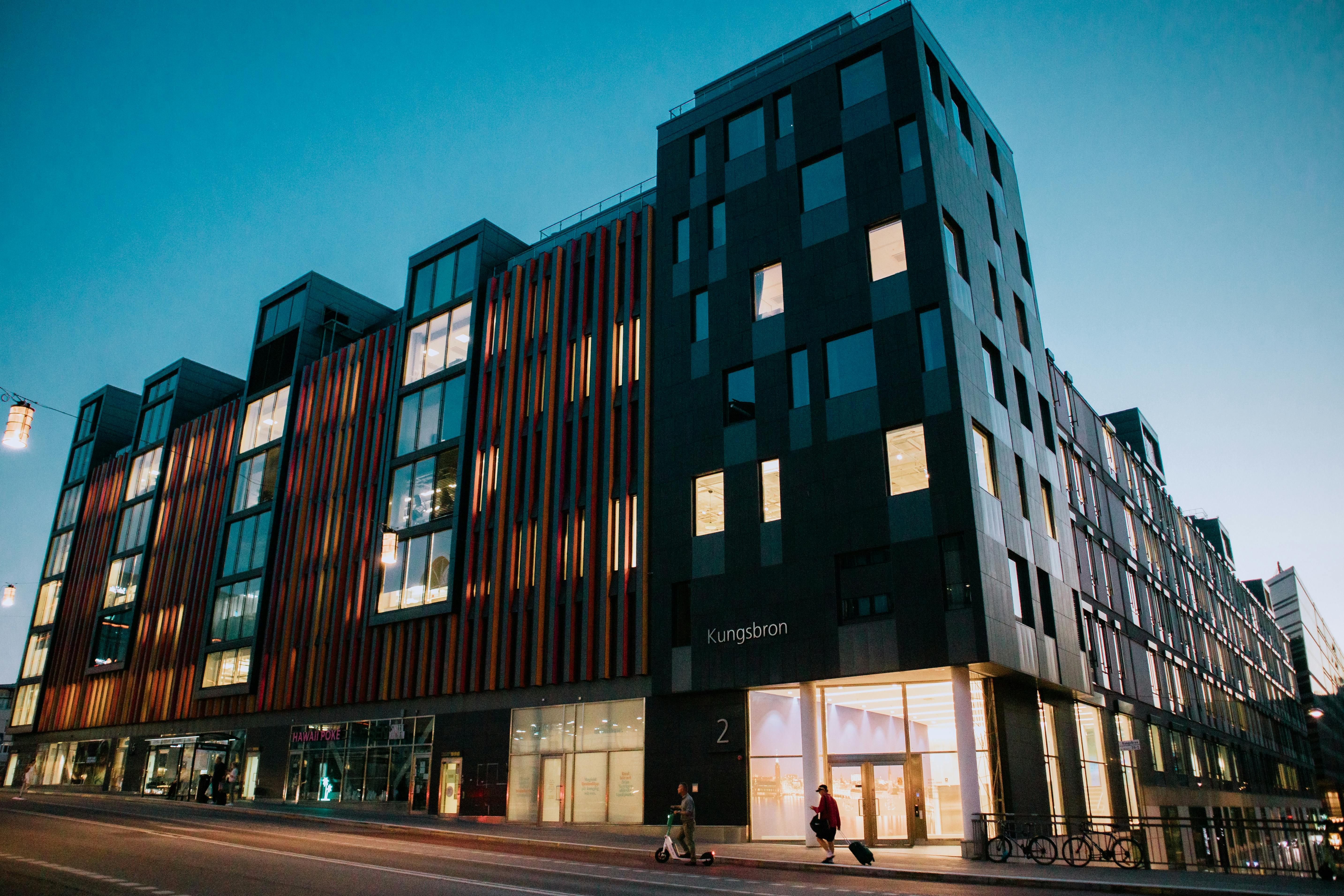 Modern commercial building with illuminated windows along a city street at dusk.