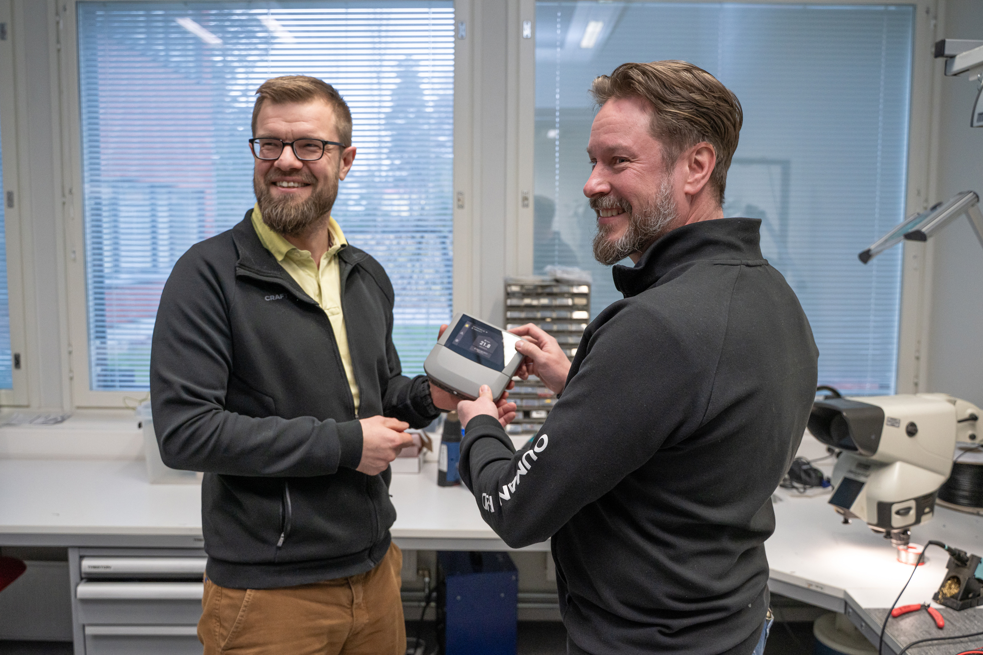 Two engineers testing and discussing a digital HVAC control device in a workshop.